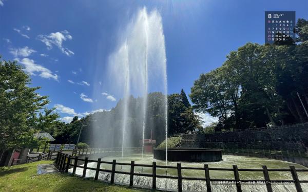 右上に令和5年8月のカレンダー、青空の下、高く水を噴き上げる円筒分水工を撮影した8月の壁紙カレンダーの写真