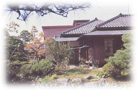 たくさんの木々が植えられ、その奥に瓦屋根の斎藤實記念館の旧宅(住居)が見えている様子を庭から写した写真