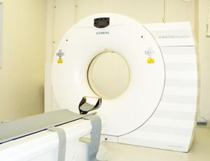 アイボリーの壁の部屋に、ドーナツ状の白い機械と検査をするためのベッドが設置されている写真