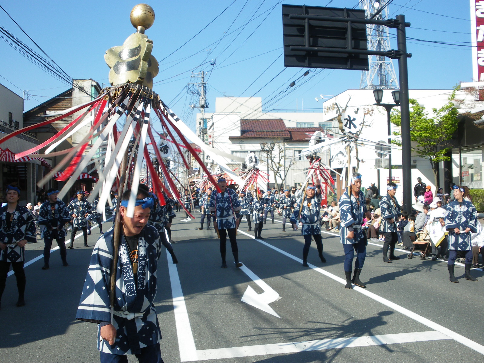 歩行者天国の道路を法被姿の消防団の方々が纏いを回しながら歩いている祭りの様子の写真