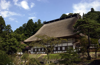 手前に木々が立つ庭園があり、奥に入母屋造で茅葺の大屋根を備えた正法寺を右斜めから撮影した写真