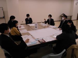 資料が広げられたテーブルを囲んで8名の参加者が話し合いをしている3班の様子を写した写真