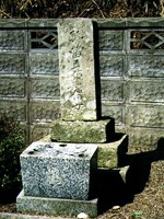 ブロック塀の前に建つ古い石のお墓を写した写真