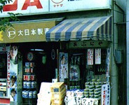 入り口付近に沢山の薬などが置かれ、黄土色の軒先テントにP大日本製薬と書かれた建物外観の写真