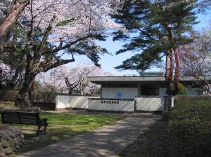 松の木や桜が植わった庭園の石畳の歩道先に、白い塀に囲まれた四角い白壁の建物がある高野長英記念館の外観写真