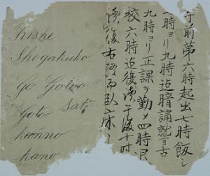 紙が薄茶色に変色しており、左側は英文、右側には漢字と片仮名で書かれた文章で、紙の周りが一部無くなっている日課を書き記した断片の写真