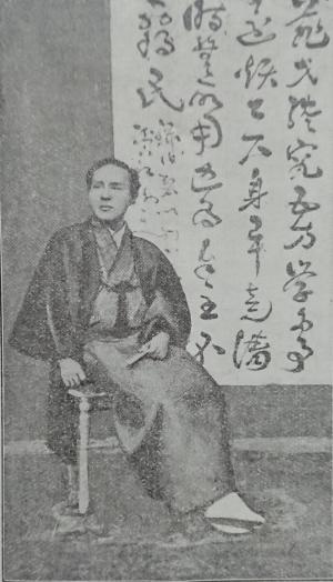 漢字で文章が書かれている大きな紙を背景に着物姿で椅子に腰かけている司馬凌海の肖像画