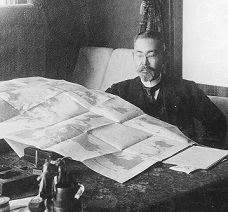 机の前に座り、大きな紙を広げて見ている満鉄時代の後藤新平氏の白黒写真