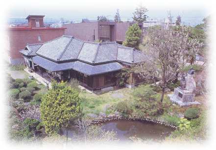 手前に池があり、中央の木々の中に日本家屋が建ち、奥には赤レンガの建物が見える斎藤實記念館の写真