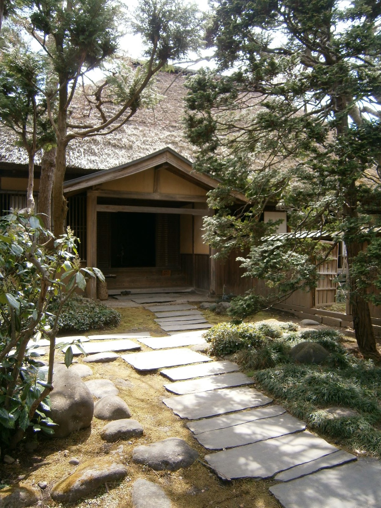 庭に石の通路がありその両脇に木々があり奥には玄関がある旧内田家住宅入口の写真