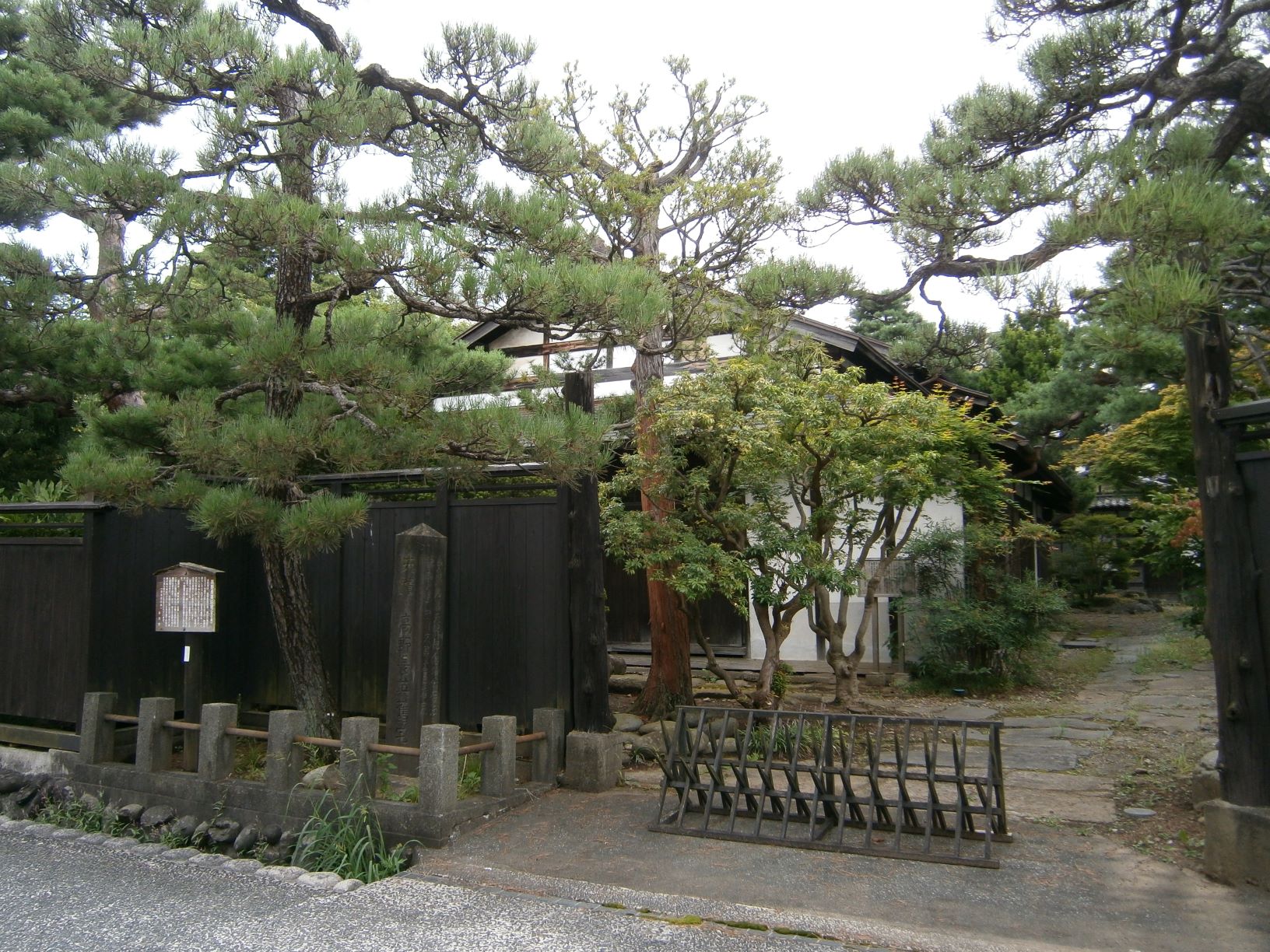 通路沿いに板張りの壁に松の木が立ち、その後ろに高野長英旧宅の外観写真