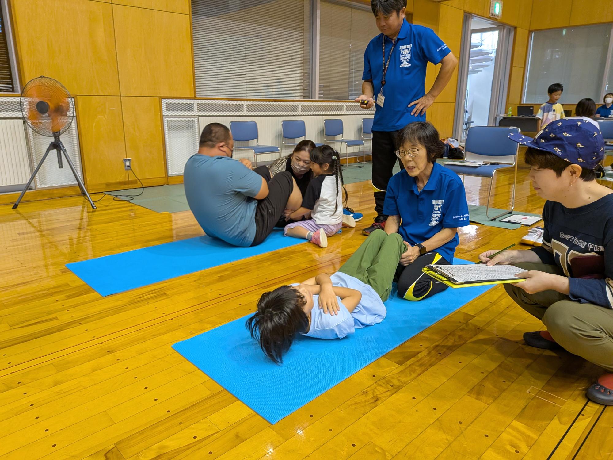 イベントに参加している小さな男の子と年配の男性に寄り添うスポーツ推進委員の女性の写真