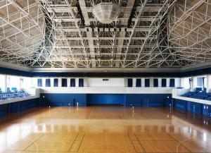 鉄骨が見えている高い天井の中央に大きな冷暖房設備が設置され、2階には観客席がある、バスケットボールコート2面の広さの江刺中央体育館内の写真