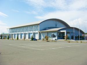 手前に広い駐車場スペースがあり、奥にアーチ状の屋根で全体が白色をした江刺西体育館の外観写真