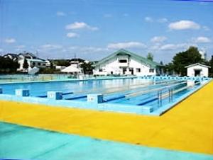 水面に青空が映った、プールサイドの床の外周が水色、内周が黄色の大鐘公園市民プールの写真