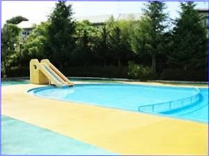 プールサイドの床の外周が水色、内周が黄色で、丸く仕切られたプールの一か所に黄色の滑り台がついた、大鐘公園市民プール 幼児プールの写真
