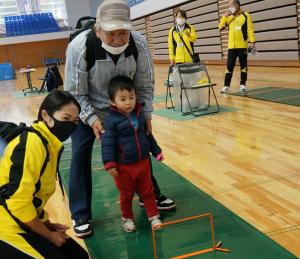 イベントに参加している小さな男の子と年配の男性に寄り添うスポーツ推進委員の女性の写真