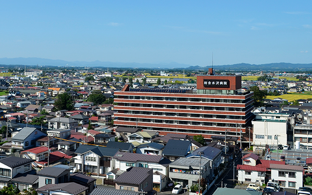 家が立ち並ぶ中央に7階建ての大きなレンガ色の外壁をした総合水沢病院の全体を写した写真
