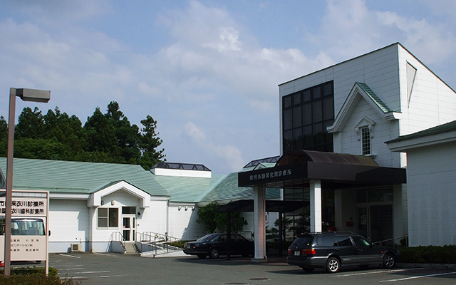 白い外壁片流れ屋根の衣川診療所入口横に車が停車し、その横に衣川歯科診療所の建物が建っている写真