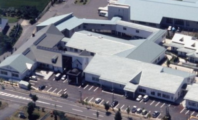 横に長く連なっている建物と、周囲に駐車場が設けられている衣川診療所の敷地内を上空から撮影した写真