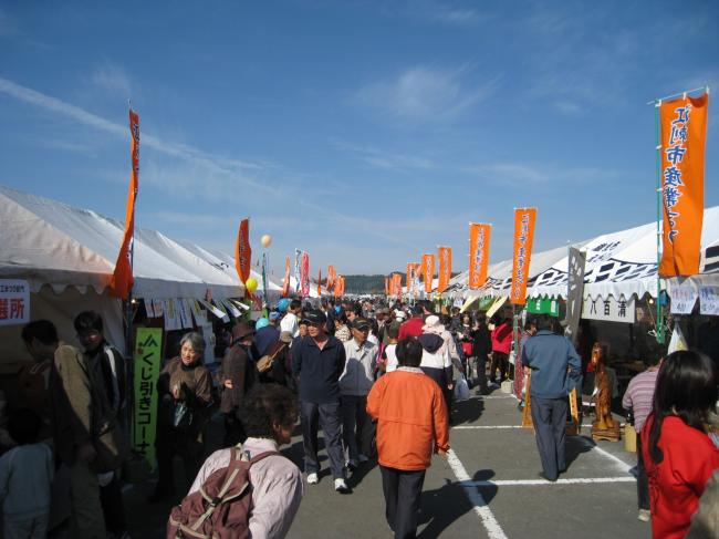 中央の通路の両脇にオレンジに青色で江刺産業まつりと書かれたのぼり旗がテントに掲げられ、たくさんの来園者の人達が見学をしている産業まつりの写真