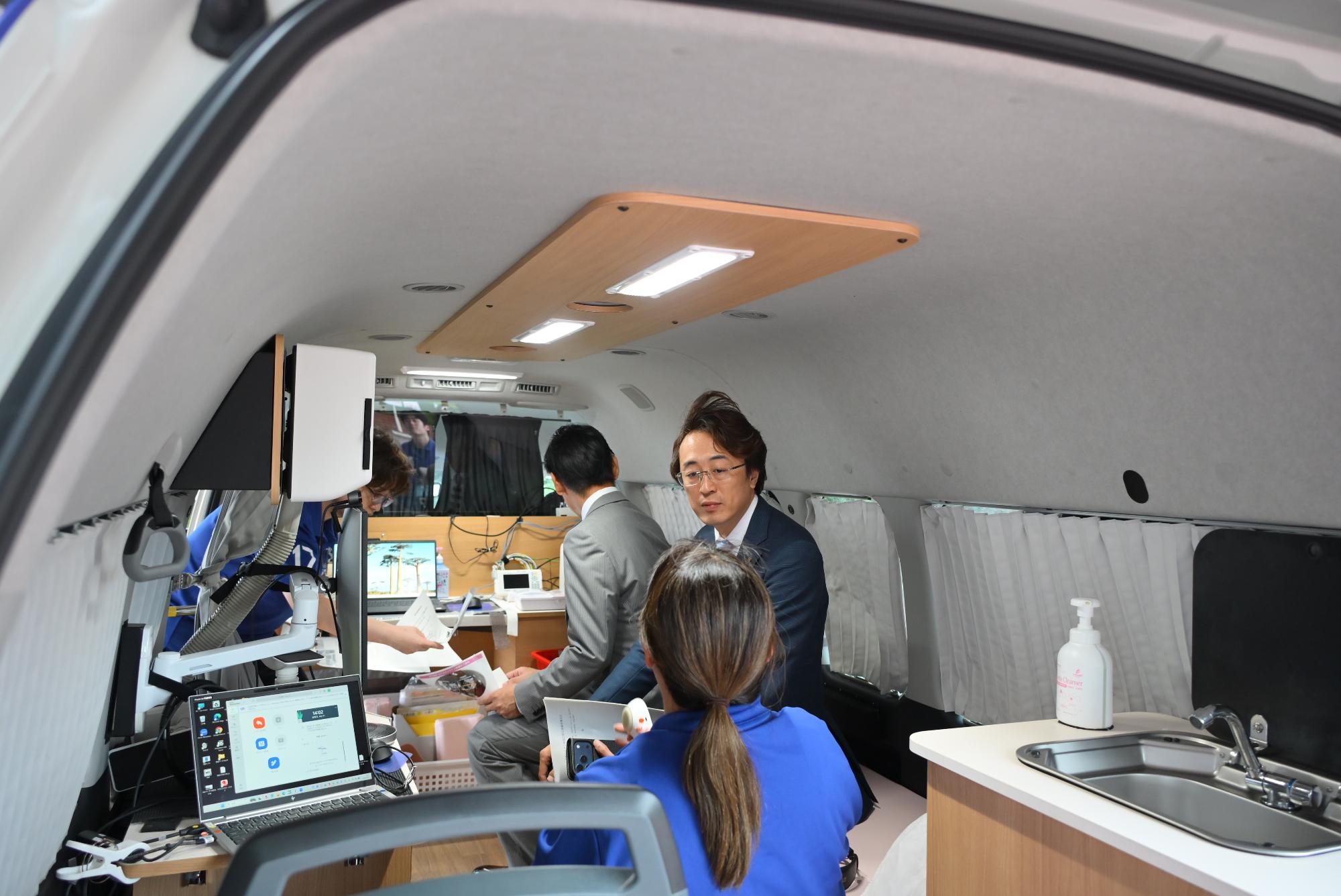 遠隔診療車の中で説明を受ける松本代表取締役と佐藤花泉工場管理部長の写真