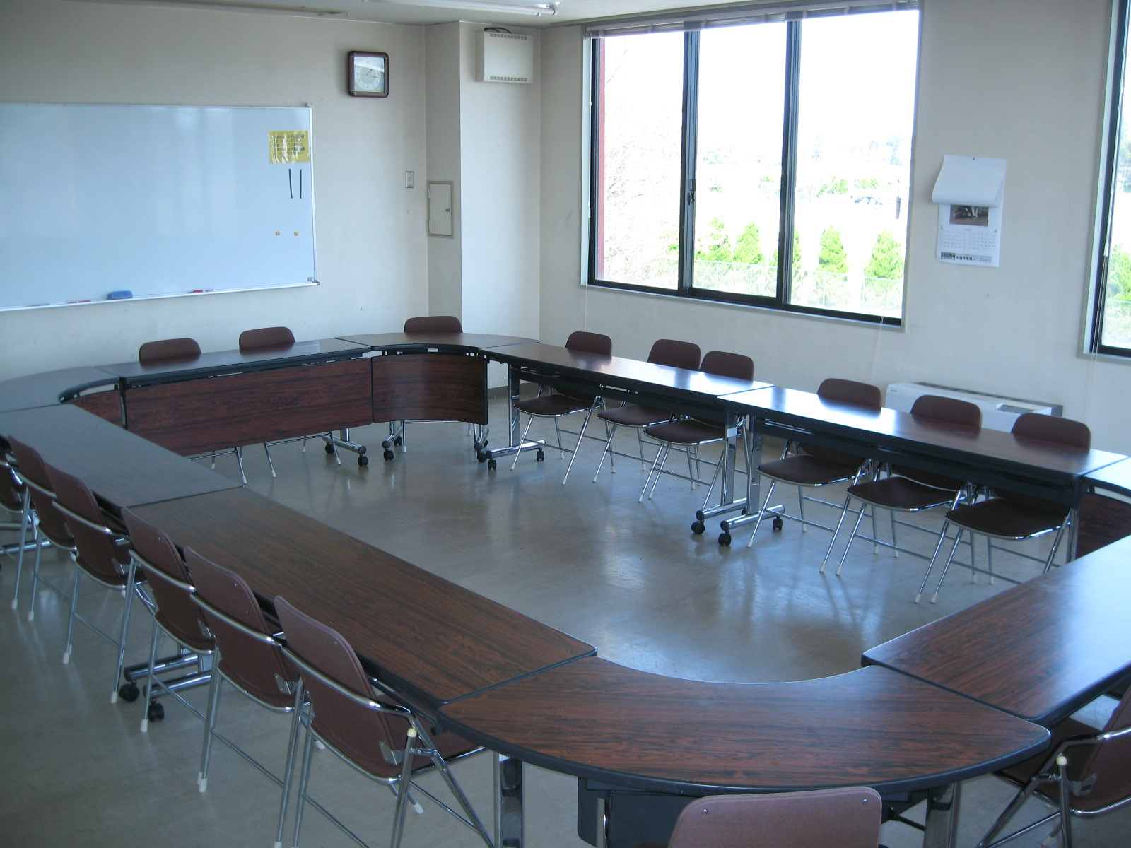 壁に設置されているホワイトボードの前に、長机が大きなロの字型に配置されている会議室の写真