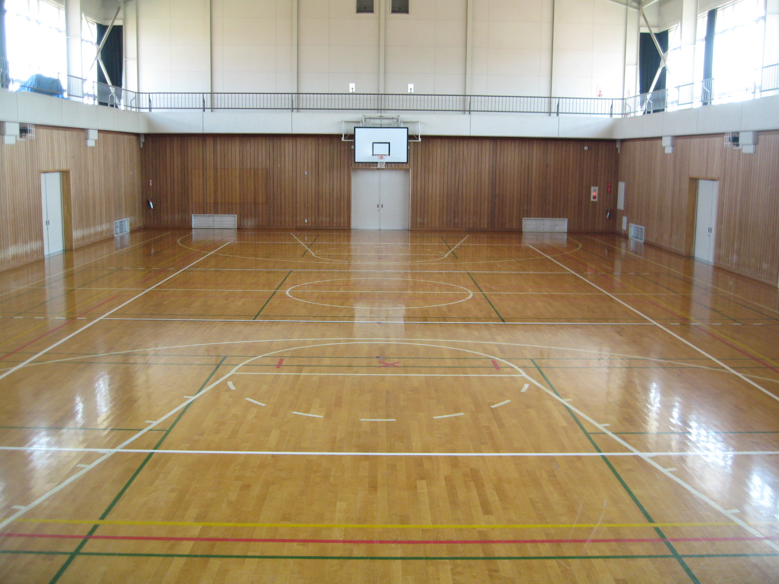 壁にバスケットゴールが設置され、床にラインテープが貼り付けてある広々とした体育館の写真