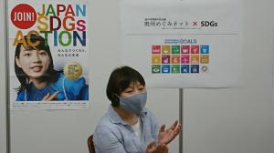 JOINI JAPAN SDGs ACTIONのポスターが飾られ、若生和江代表が説明をしている様子を写した写真