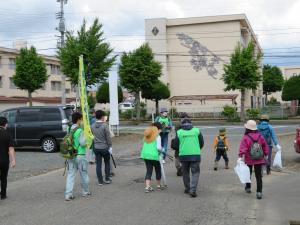 黄色いのぼり旗を持った方、蛍光色の黄緑色のベストを着た方、ごみ袋を持った参加者達が宇宙遊学館へ向かって歩き出した後ろ姿を写した写真