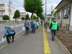 参加者達が縦に並んで道路横の歩道を歩きながらごみを拾っている写真