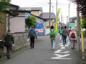 住宅街の中を歩いてごみ拾いをしている参加者達の後ろ姿を写した写真