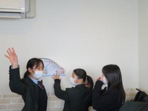 女子生徒たちが、壁にポップを貼ろうとしている様子と、一名の女子生徒が手振りをつけて話す様子の写真