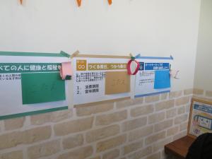 壁に緑と黄色と水色の3枚のポップが展示され、それぞれのポップの一部分に「こたえ」と書かれた紙を上から貼っている写真
