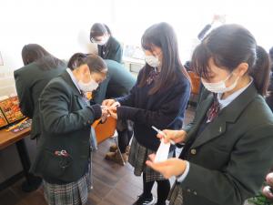 机の上で作業をしている女子生徒たちと、紙を手に持って作業をしている女子生徒たちの写真