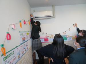 壁に貼られたポップの周りに糸に通した画用紙の飾りを貼り付けている女子生徒や、それを周りから見守る生徒たちの写真
