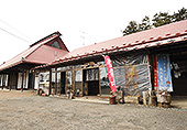 木造に赤茶色の瓦屋根の平屋と、三角屋根の建物が並んで立っている、「農家レストラン まだ来すた」の外観写真
