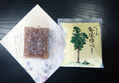 紙の上においてある長方形で茶色の角塚ゆべしと、「いさわ角塚ゆべし」の文字と一本杉のイラストが描かれた菓子袋の写真