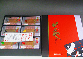 6つに仕切られた黒い箱に種類の違うおせんべいが詰められ、横に中央の広い部分が赤色、左端が黒、右端が白のデザインで「せんや」と金色の文字が書かれた箱の蓋が置かれている写真