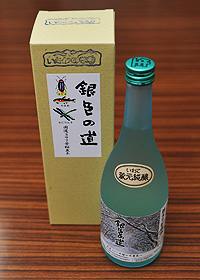 銀色の道のラベルの貼られた箱とエメラルドグリーンのガラス瓶に店主の風景画が印刷された「銀色の道」のオリジナルラベルの貼られた日本酒「銀色の道」の商品の写真