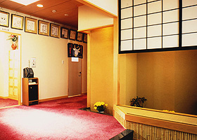 和風の内装の廊下に赤いじゅうたんが敷かれ、壁の上部には色紙の入った額がたくさん飾られている、「ささ忠」玄関付近の写真