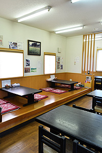 黒い木目のテーブルが置かれた板張りの座敷とテーブル席がある「そば処もちた屋」の店内の写真