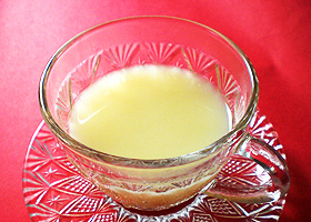 赤いテーブルの上に置かれているガラスのティーカップに注がれたリンゴ甘酒の写真