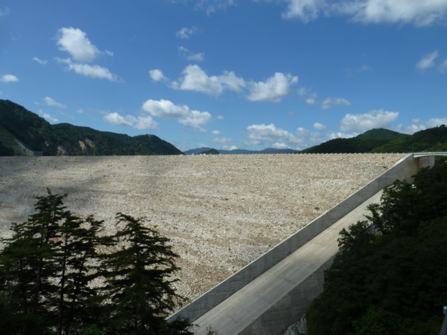 上空の雲の影がダムに写っている、山並みに囲まれた胆沢ダムの写真