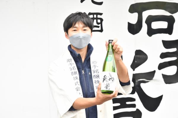「奥州ノ龍」と書かれたラベルが貼られた焼酎瓶を持っている岩手銘醸株式会社 専務取締役 及川順也さんの写真