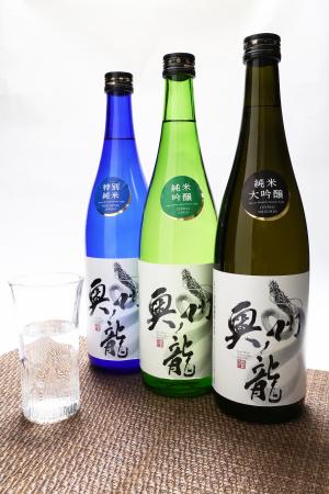 黒、緑、青色の3本の瓶に奥州ノ龍のラベルが貼られ、ガラスコップに日本酒が注がれている写真