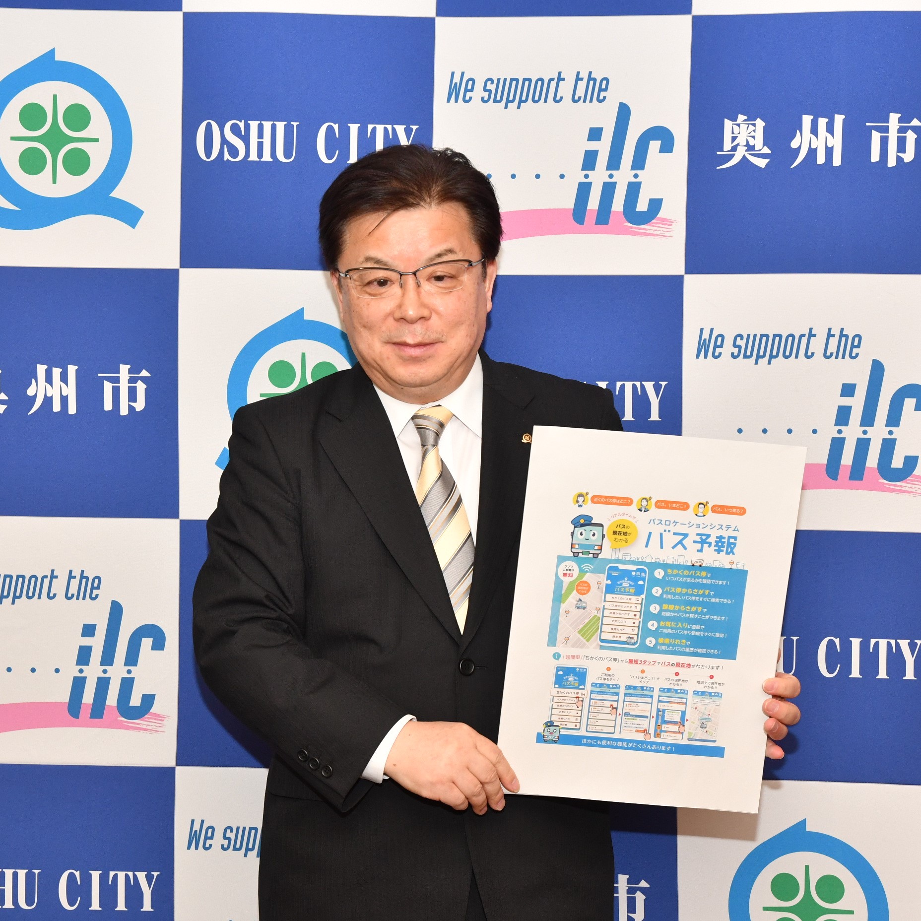 「バス予報」のチラシパネルを持つ倉成市長