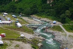 周辺に青々とした木々が立ち並び、地形を活かしたコースの川の水が勢いよく流れているいさわカヌー競技場の様子を上空から写した写真