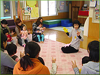 手袋人形を付けた職員と子どもを膝に座らせた母親が一緒に手遊びをしている写真