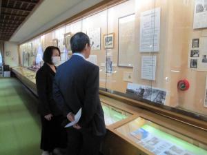 ショーケースにずらりと資料が展示されている記念館で、水内大使と女性が展示資料の方を見ながら鑑賞している様子の写真